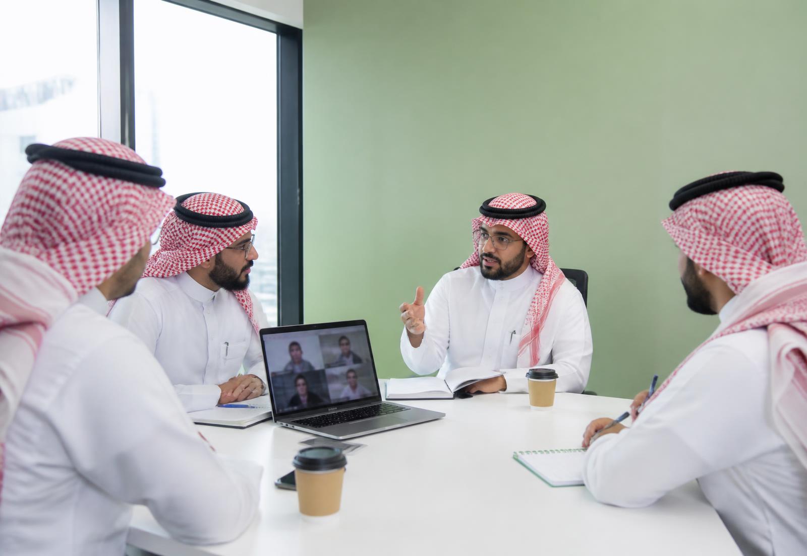 فريق هندسي في اجتماع بمكتب حديث مع حاسوب محمول يعرض مكالمة مرئية